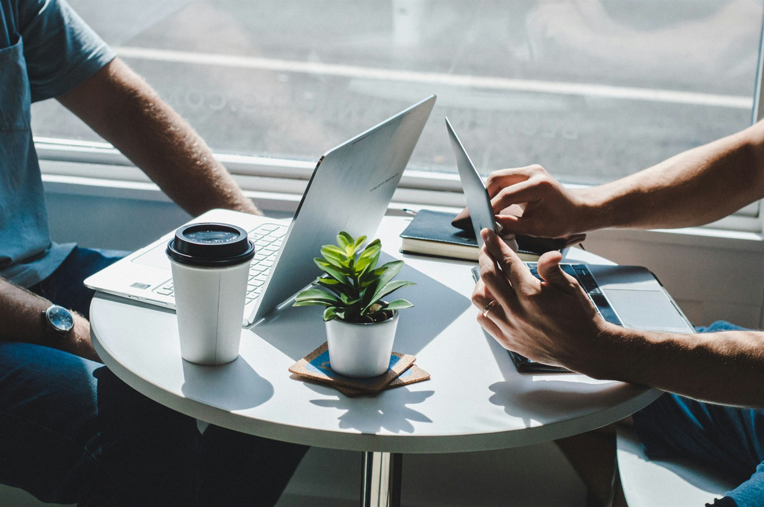 Two people reviewing designs across a small table with laptops and coffee